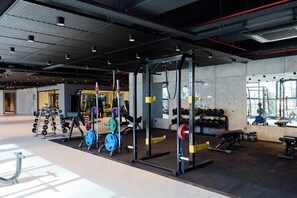 A modern gym with weightlifting equipment, cardio machines, and a large window providing natural light.