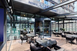 Moderni ulkotila, jossa on pöytiä ja tuoleja, lasinen sisäänkäynti ja kyltti, jossa lukee: ”Bonnuti Arjaam by Rotana”.