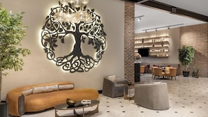 A modern living area with a sofa, ottoman, and coffee table, a decorative wall piece, and a kitchen area in the background. - Bomonti Suites (Istanbul)