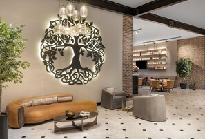 A modern living area with a sofa, ottoman, and coffee table, a decorative wall piece, and a kitchen area in the background. - Bomonti Suites (Istanbul)