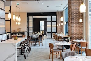 A modern restaurant interior with a marble bar, wooden tables, and hanging pendant lights.