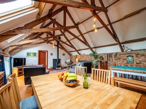 Ein rustikales Interieur mit sichtbaren Holzbalken, einem Kamin, einem Billardtisch und einem Essbereich mit Obst und Wein.