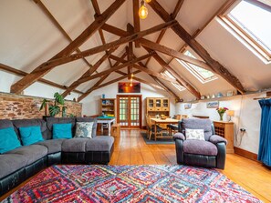 Ein Loft-Zimmer mit freiliegenden Holzbalken, einem großen Fenster, einer Couch, einem Sessel und einem Esstisch.
