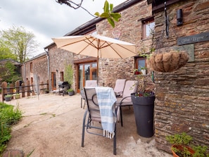 Ein Steinhaus mit einer Terrassenfläche, die Sitzgelegenheiten im Freien, einen Grill und Topfpflanzen bietet.