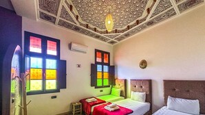 A hotel room with two beds, a large window with colorful panes, a patterned ceiling, and a traditional lamp. - Riad Malayine Sarl (Marrakech)