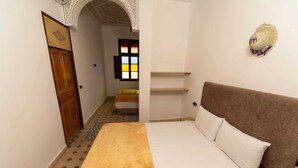 A bedroom with a bed, a wooden door, a window with colorful panes, and a decorative wall piece. - Riad Malayine Sarl (Marrakech)