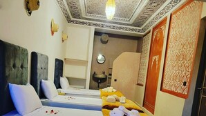 A hotel room with two beds, a small sitting area, a bathroom with a sink, and decorative wall patterns. - Riad Malayine Sarl (Marrakech)