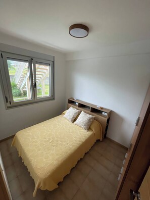 Un dormitorio con una cama, dos almohadas, un cabecero, una ventana y una puerta.