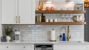 A modern kitchen with white cabinets, stainless steel appliances, and wooden shelves. - Beach Daze | Beachfront, Heated Outdoor Pool,  Newly Renovated! (Traverse City)