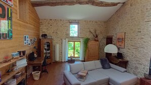 Une pièce rustique avec un mur en pierre, des meubles en bois, une bibliothèque et une fenêtre avec des rideaux.