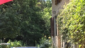 Un bâtiment en pierre avec une piscine, entouré de verdure et agrémenté d’un parasol rouge.