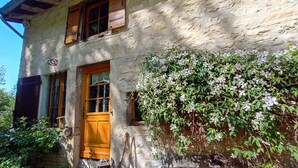 Un bâtiment rustique en pierre, doté d’une porte en bois, de fenêtres et d’un mur recouvert de plantes grimpantes.
