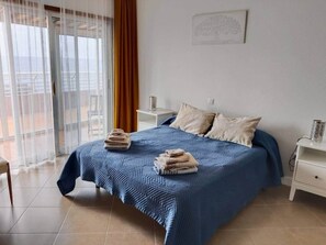 A bedroom with a bed, a nightstand, a chair, a window with curtains, and a balcony view. - Seaview Muelle en pleno centro, Puerto de la Cruz (Puerto de la Cruz)