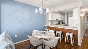 Een moderne keuken met witte kastjes, een centraal eiland en een eethoek met een ronde tafel en witte stoelen.