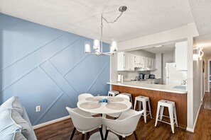 A modern kitchen with white cabinets, a central island, and a dining area with a round table and white chairs. - Beautifully Upgraded!  Pool and Beach Access (North Myrtle Beach)