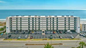 Een meerhoog hotel met een parkeerplaats ervoor, gelegen nabij een strand.