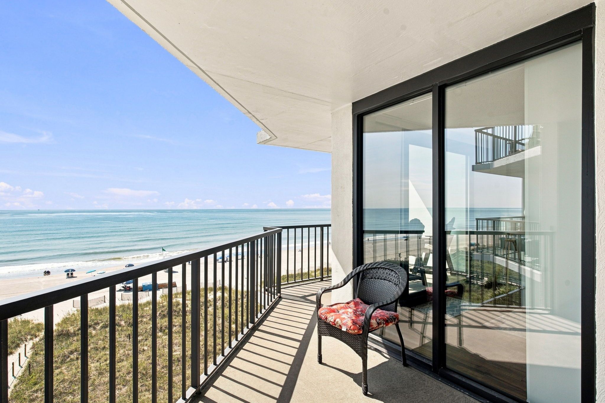 Un balcon donnant sur la plage et l’océan, une chaise et une porte vitrée qui mène à un espace intérieur.