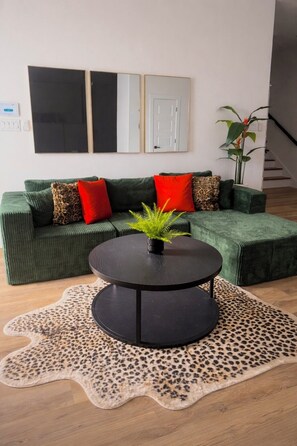 Ein modernes Wohnzimmer mit einem grünen Sofa, einem runden schwarzen Couchtisch und einem Leopardenfell-Teppich.