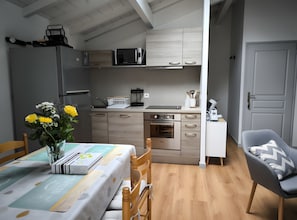 A compact kitchen with modern appliances, a dining area with a table set for two, and a cozy seating area. - Apartment 'Gîte Peyo Saint-Pée-sur-Nivelle' with Mountain View, Shared Garden and Wi-Fi (Saint-Pée-sur-Nivelle)