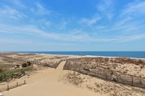 Ein sandiger Strand mit einer Holzzaun, einem klaren Himmel und dem Meer im Hintergrund.