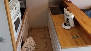 Ett kompakt kök med en inbyggd ugn, en kaffemaskin och en bänkskiva i trä.