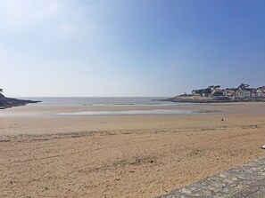 A beach with a stone walkway, a clear sky, and buildings in the background.