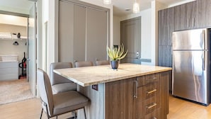 A modern kitchen with a central island, stainless steel refrigerator, and pendant lighting. - Landing Furnished Apartments near UT Arlington (Arlington)
