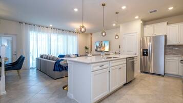 A modern kitchen with white cabinetry, stainless steel appliances, and pendant lighting.