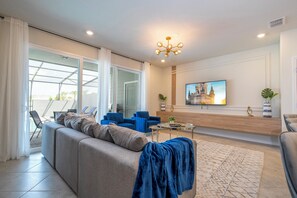 Ein modernes Wohnzimmer mit einer Couch, blauen Sesseln, einem Couchtisch und einem an der Wand befestigten Fernseher.