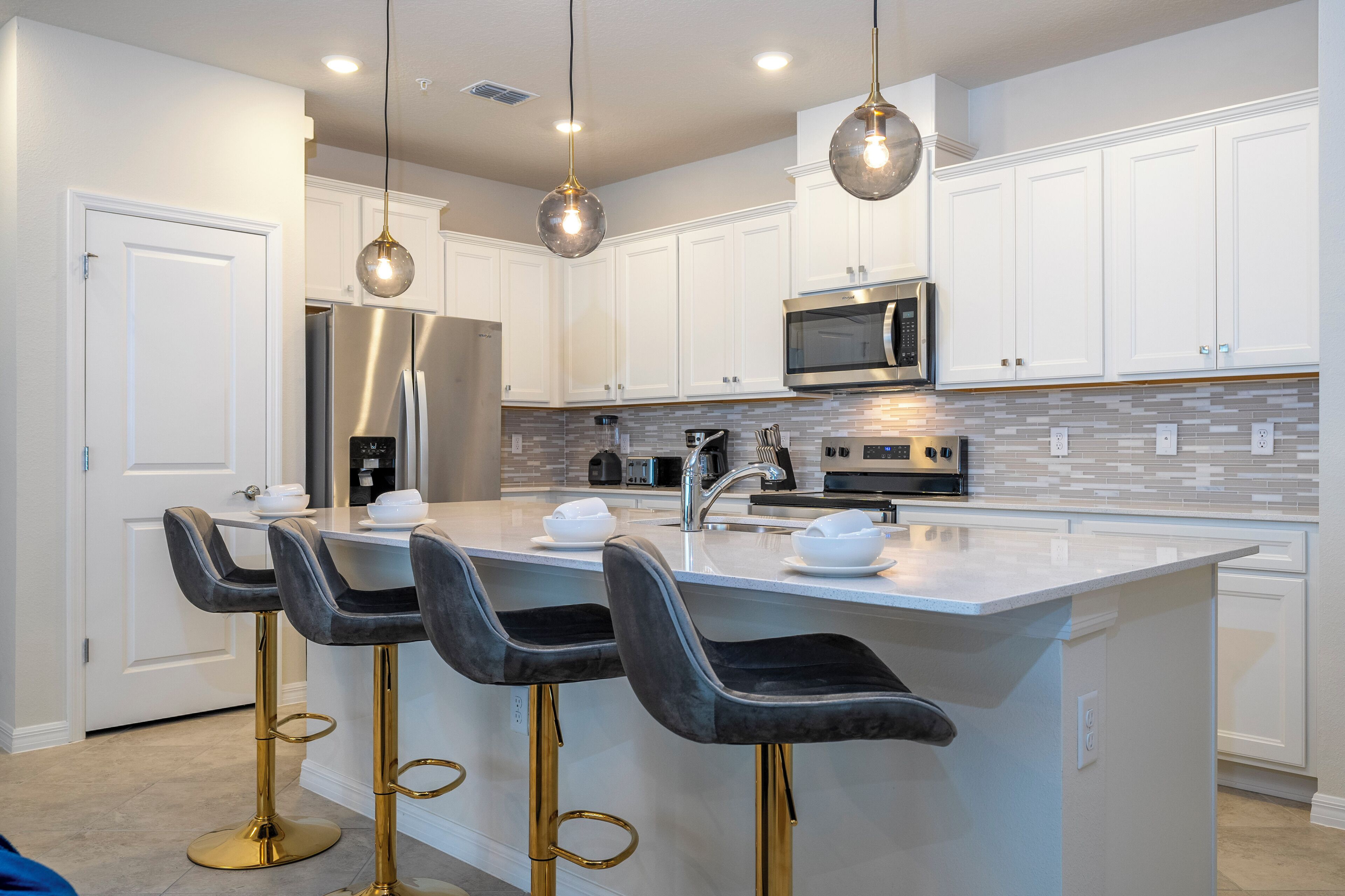 A modern kitchen with white cabinets, a stainless steel refrigerator, a microwave, and a large island with bar stools.