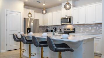 A modern kitchen with white cabinets, a stainless steel refrigerator, a microwave, and a large island with bar stools.