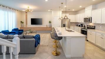 A modern kitchen with white cabinets, a central island, and a dining area with a sofa and chairs.
