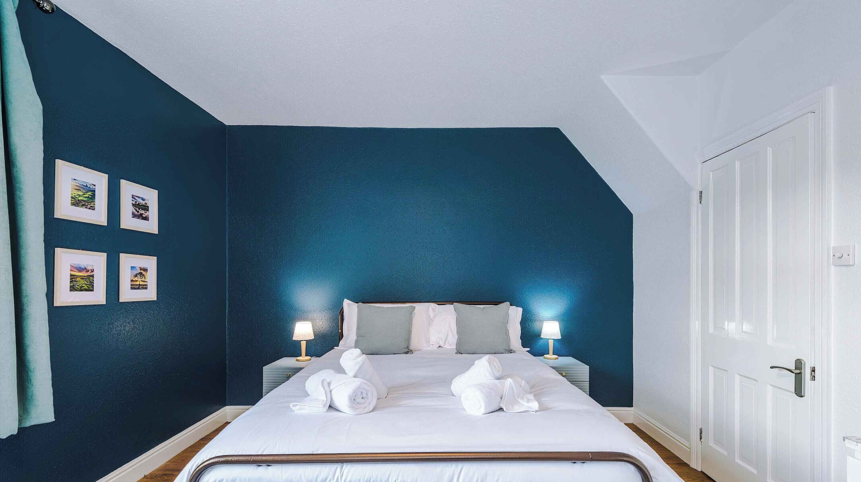 A bedroom with white bedding centered against a deep blue accent wall.