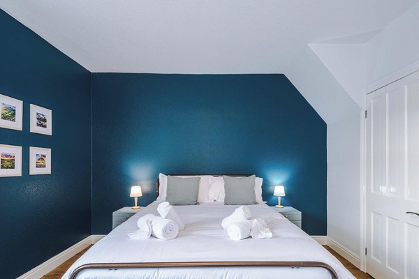 A bedroom with white bedding centered against a deep blue accent wall.