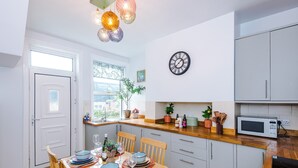 Ett kök med ett matbord för fyra personer, en klocka på väggen och ett fönster med utsikt över grönområden.