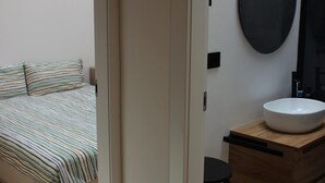 A bedroom with a bed, a bedside table, a mirror, and a bathroom with a sink and a towel rack. - Bright Design Loft - Milan Certosa District (Milano)