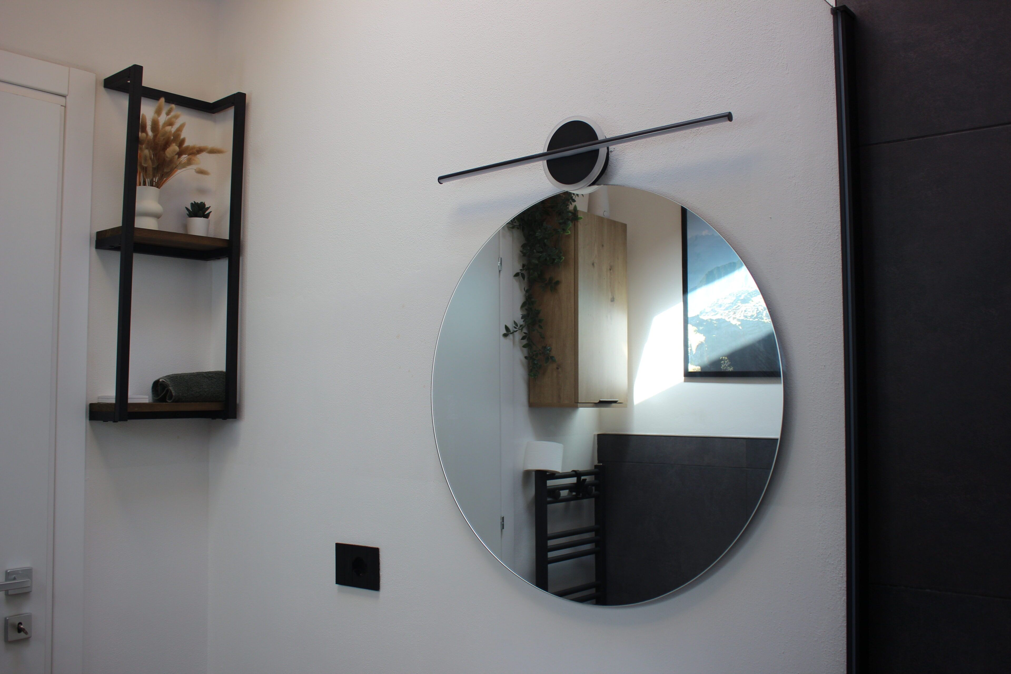 Een kamer met een ronde spiegel, een plank met decoratieve objecten en een deur.