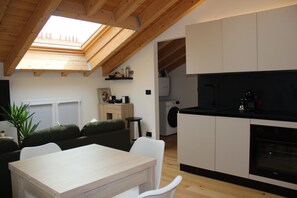 A modern kitchen with a skylight, a dining area with a table and chairs, a sofa, and a washing machine in the background. - Bright Design Loft - Milan Certosa District (Milano)