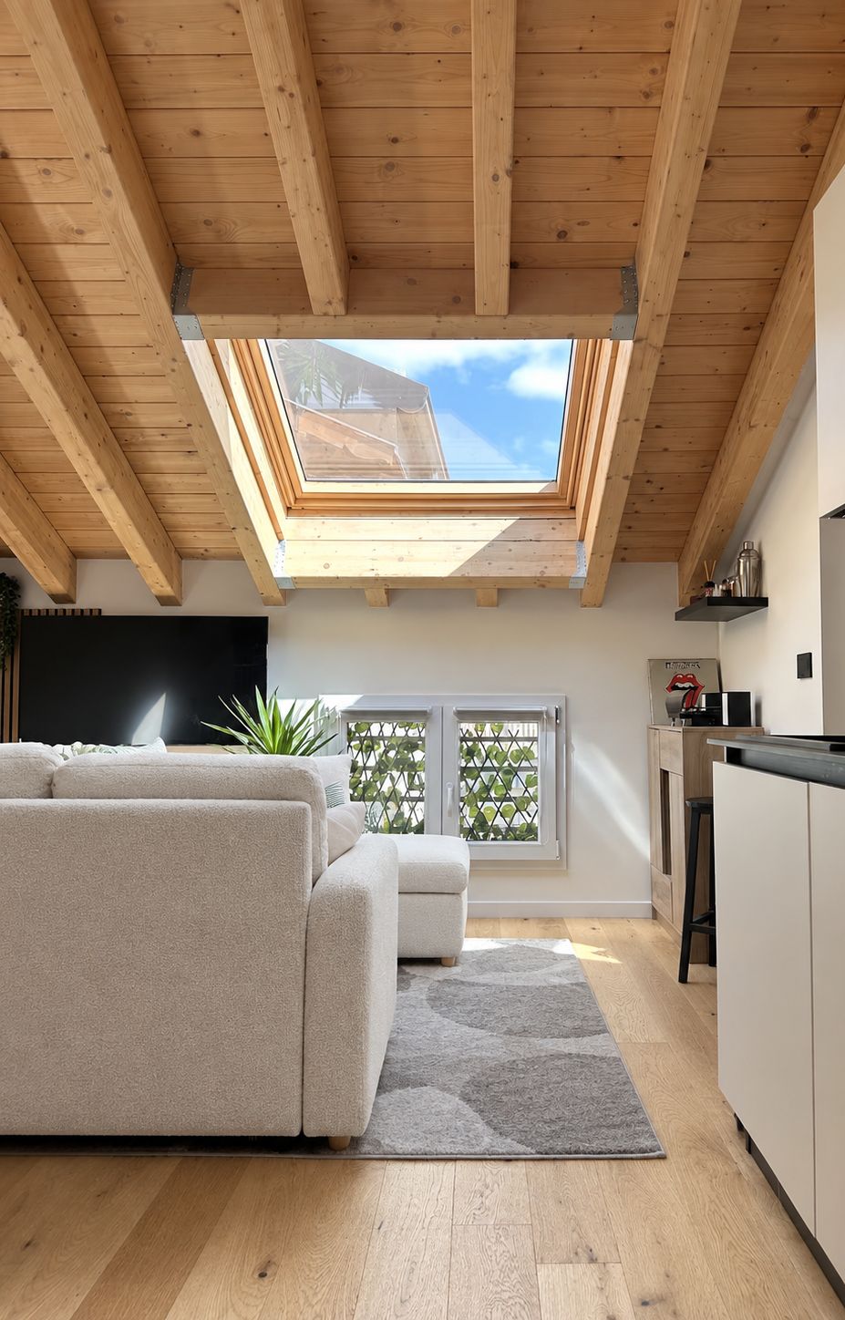 Un intérieur moderne avec un plafond en bois, une lucarne, un canapé, un coin cuisine et un téléviseur.