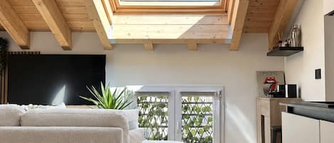Un interior moderno con techo de madera, tragaluz, sofá, zona de cocina y televisor.