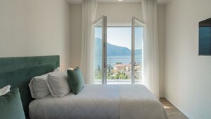 Ein Schlafzimmer mit Bett, Blick auf ein Gewässer und Gebäude, sowie einem Fenster mit Vorhängen.