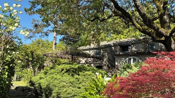 A stone building with a traditional design, surrounded by lush greenery and trees.