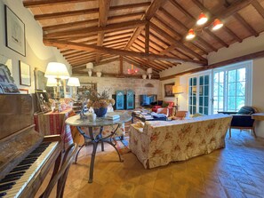 Un salon spacieux avec un plafond en bois, un piano, une table ronde ornée d’un vase et un canapé.