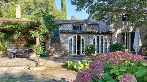 A stone building with arched windows and a garden with hydrangeas.