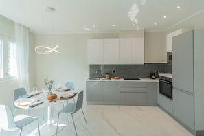 Een moderne keuken met een eethoek, met een marmeren aanrechtblad, grijze kastjes en een bijzondere hanglamp.