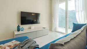 Une chambre d’hôtel moderne dotée d’une grande télévision, d’un canapé, d’une fenêtre offrant une vue sur les montagnes et d’un balcon.