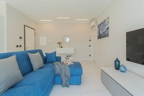 Een moderne woonkamer met een blauwe bank, een witte console tafel, een flatscreen televisie en een schilderij aan de muur.