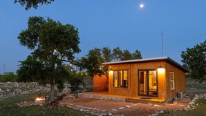 A small wooden cabin with a glass door entrance, a stone pathway, and a tree with string lights. - Cedar Haus - king bed and soaking tub (Marble Falls)