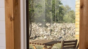 A wooden-framed window with a view of an outdoor seating area. - Cedar Haus - king bed and soaking tub (Marble Falls)