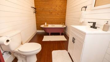 A bathroom with a white toilet, a wooden wall, a pink bathtub, and a white sink with a mirror above it.